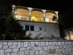 Ein zweistöckiges Gebäude mit Naturstein-Fassade, zahlreichen Fenstern mit Fensterläden und einem Balkon mit Geländer.