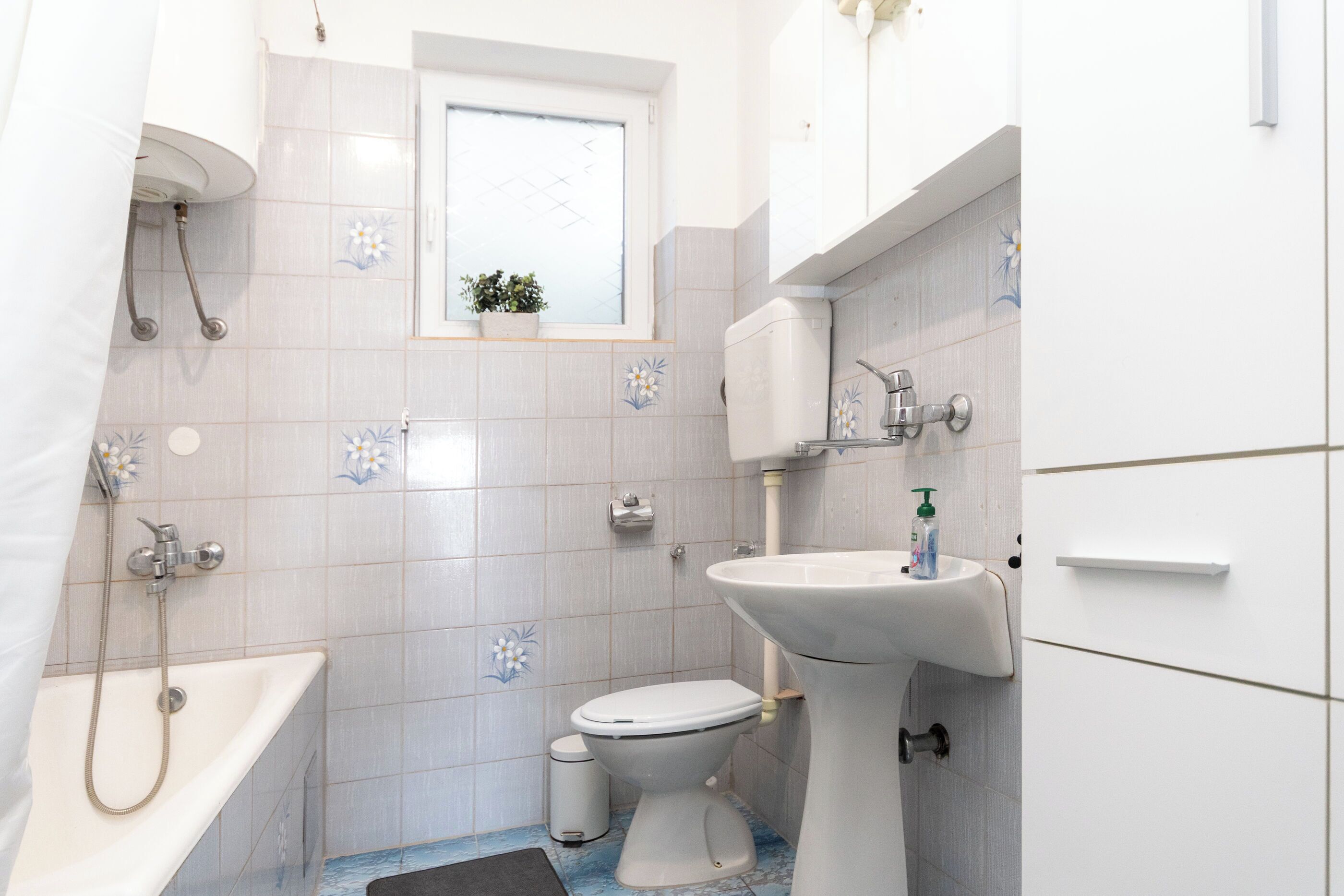 A bathroom with a toilet, sink, shower, and a small window with a plant.