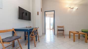 A room with a dining table, chairs, a TV, a light fixture, and a door leading to another room.