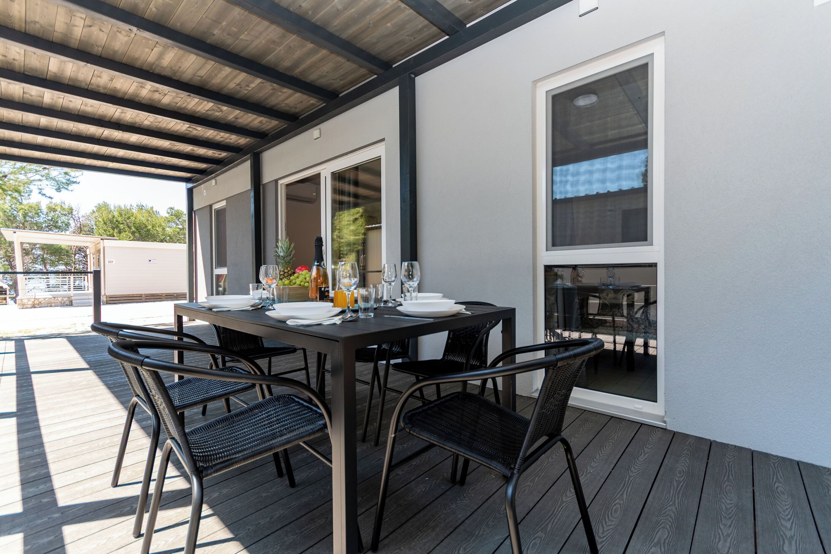 Une terrasse extérieure avec une table dressée pour quatre personnes, entourée de chaises, et un espace abrité offrant une vue sur le jardin arrière.
