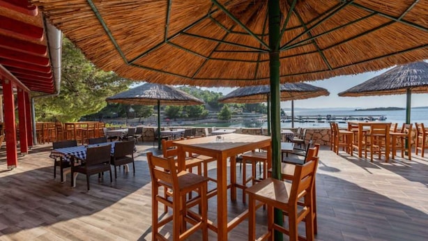 Un espace de restauration en plein air avec des tables et des chaises en bois, des parasols en chaume et une vue sur la mer.