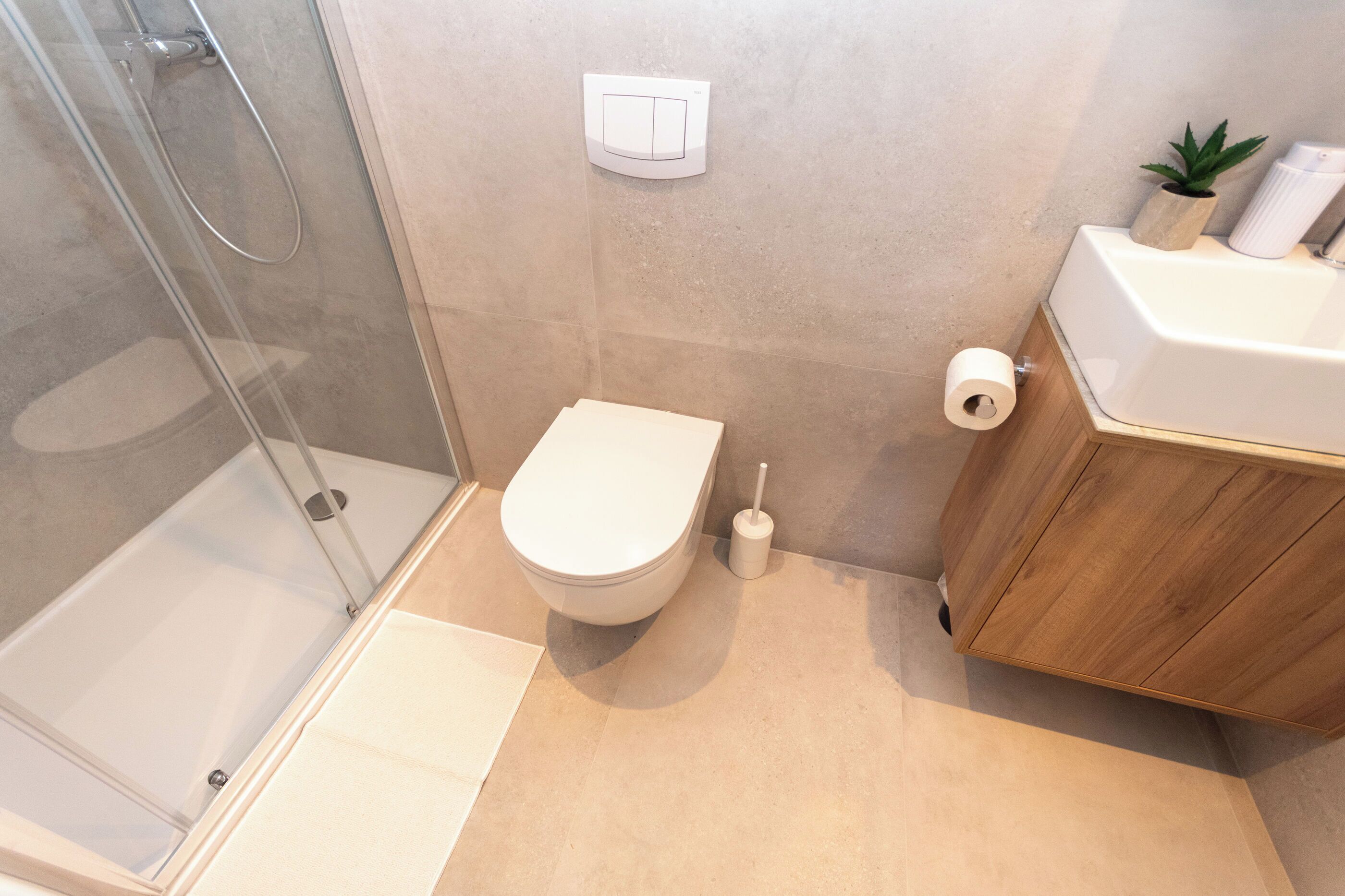 A modern bathroom with a glass shower enclosure, a toilet, and a wooden vanity with a sink.