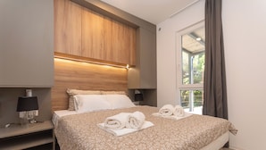 Une chambre d’hôtel moderne avec un grand lit, une tête de lit en bois, des lampes de chevet et une vue sur la verdure.