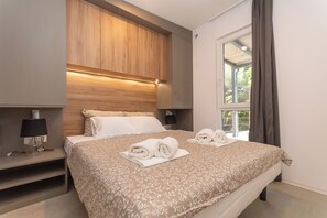 A modern hotel room with a large bed, wooden headboard, bedside lamps, and a view of greenery outside. - Mobile Home Oaza Mira Camping 920 (Pakostane)