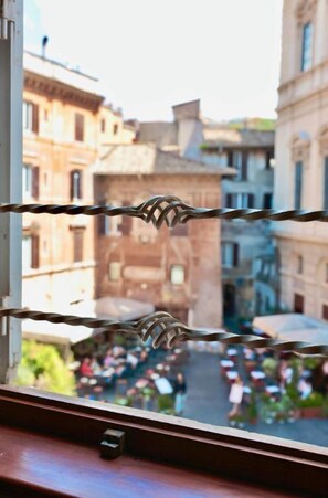Ein Fenster mit Metallgeländer, Blick auf eine Straße mit Gebäuden und eine Menschenmenge.