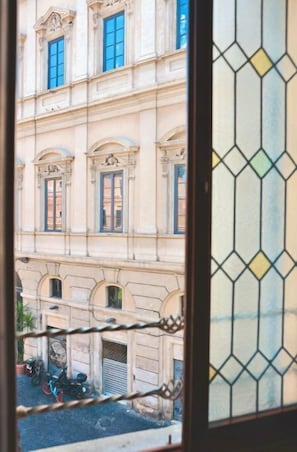 Ein Gebäude mit Rundbogenfenstern und einer Tür, sichtbar durch ein Fenster mit geometrischem Muster.