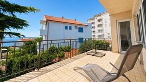 A balcony with a chair, a tiled floor, and a view of a building with a red roof. - Apartment Visnja (Crikvenica)