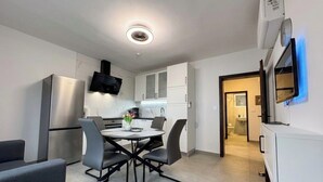 A modern kitchen with a built-in oven, a dining table with chairs, and a TV mounted on the wall. - Apartment Visnja (Crikvenica)