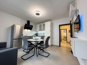 A modern kitchen with a built-in oven, a dining table with chairs, and a TV mounted on the wall. - Apartment Visnja (Crikvenica)