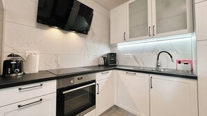 A modern kitchen with white cabinets, a black countertop, a built-in oven, a coffee maker, and a TV mounted above the counter. - Apartment Visnja (Crikvenica)