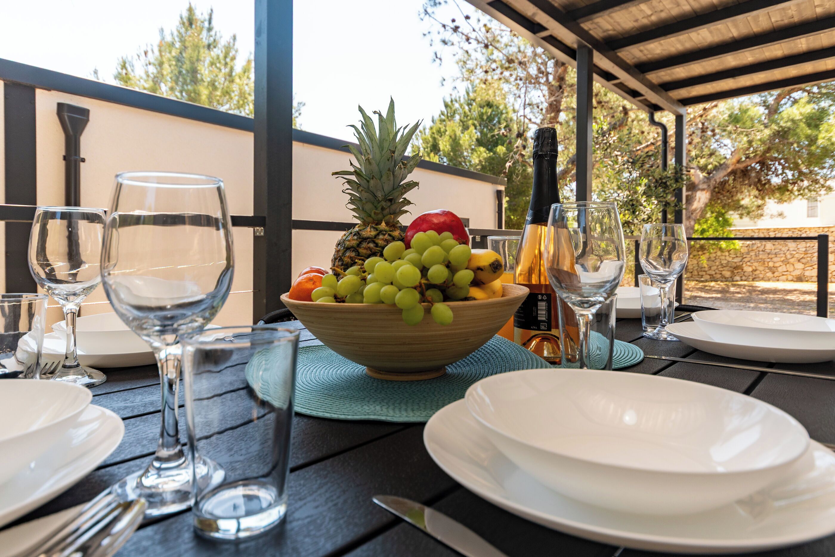 Een tafel buiten gedekt met een schaal fruit, wijnglazen en borden.