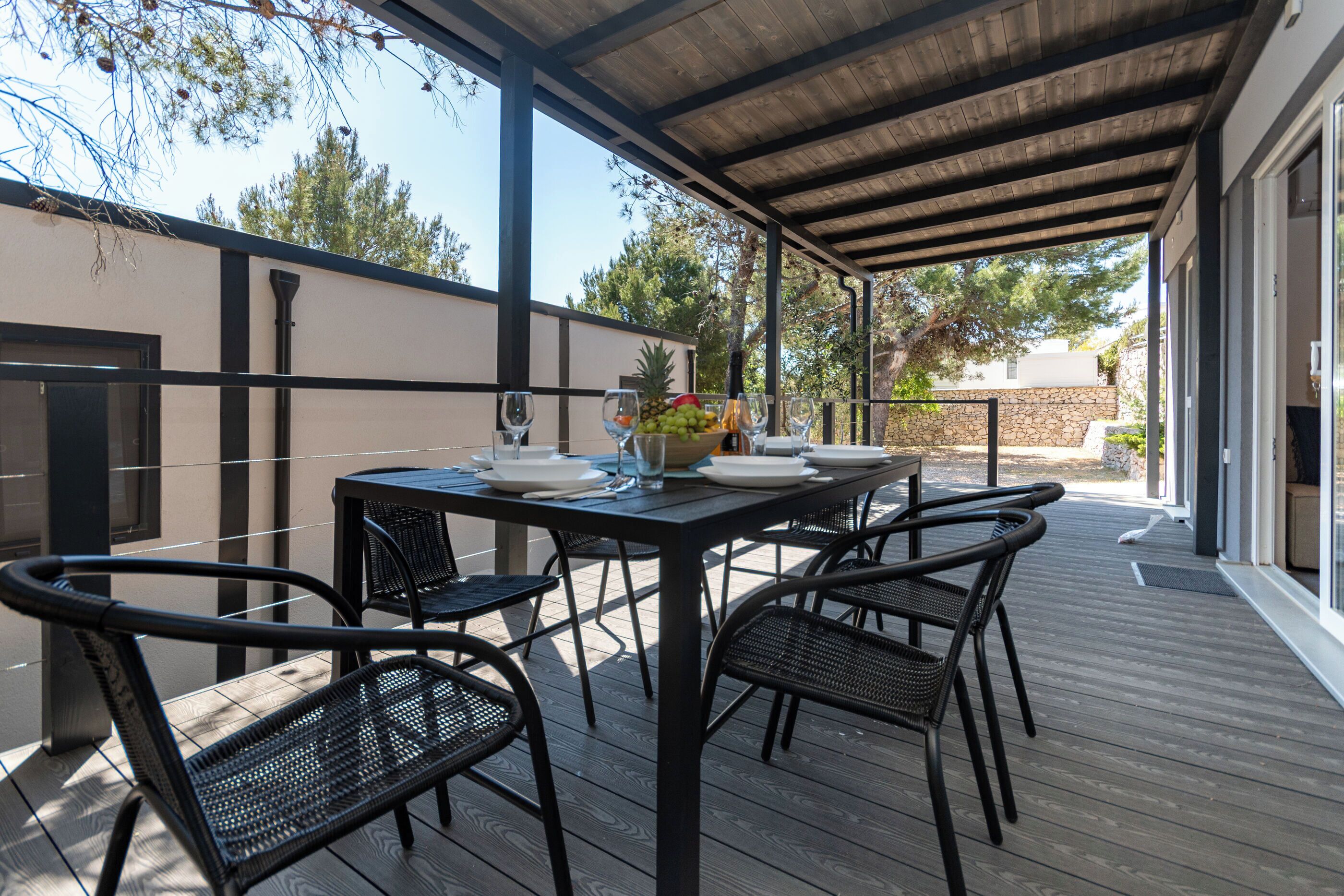 Una terrazza esterna con un tavolo apparecchiato per due persone, circondata da sedie e una ciotola di frutta sul tavolo.