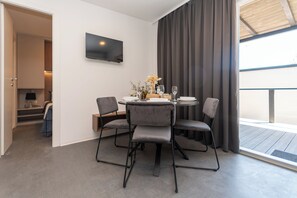 A dining area with a table set for four, a flat-screen TV mounted on the wall, and a view of the outdoors through a large window. - Mobile Home Oaza Mira Camping 904 (Pakostane)