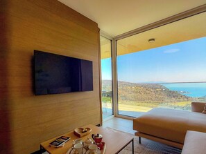 Une chambre d’hôtel moderne dotée d’une grande fenêtre, d’un téléviseur à écran plat, d’un canapé, d’une table basse et d’un ensemble de meubles pour la salle à manger.