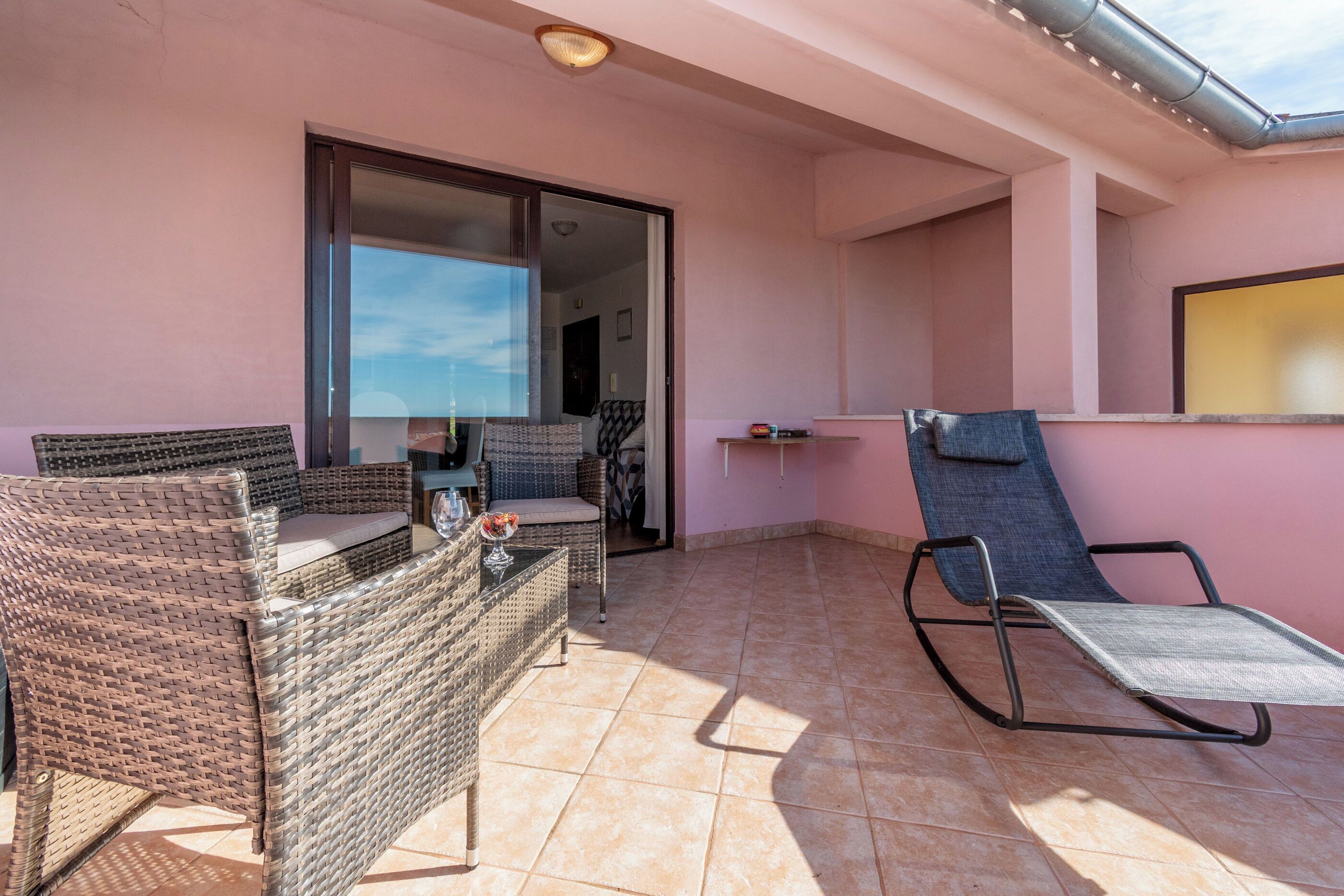 A balcony with wicker furniture, a metal chair, and a tiled floor.