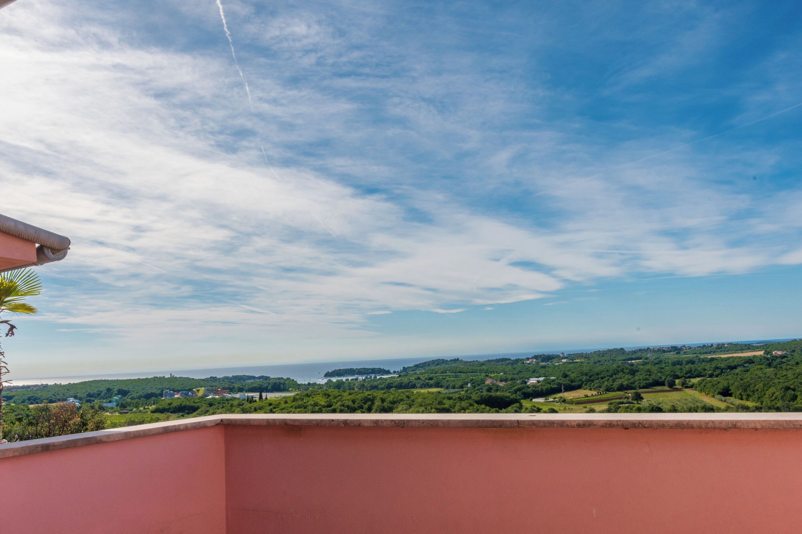 Uma varanda com vista desobstruída para a paisagem costeira, incluindo vegetação e edifícios ao longe.