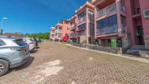 Reihenweise rosa Gebäude mit Balkonen, eine gepflasterte Straße und parkende Autos.
