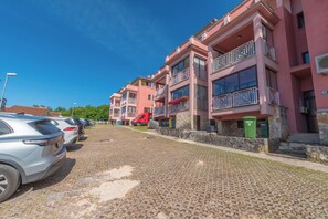 A row of pink buildings with balconies, a cobblestone street, and parked cars. - Apartment Nikola (Porec)