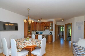 A dining area with a table, chairs, and a chandelier. There is a kitchen in the background with wooden cabinets and appliances. - Apartment Nikola (Porec)