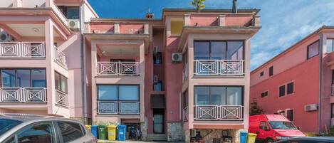 Un edificio residencial de varios pisos con balcones, una furgoneta roja estacionada frente a él y un coche aparcado en la calle.