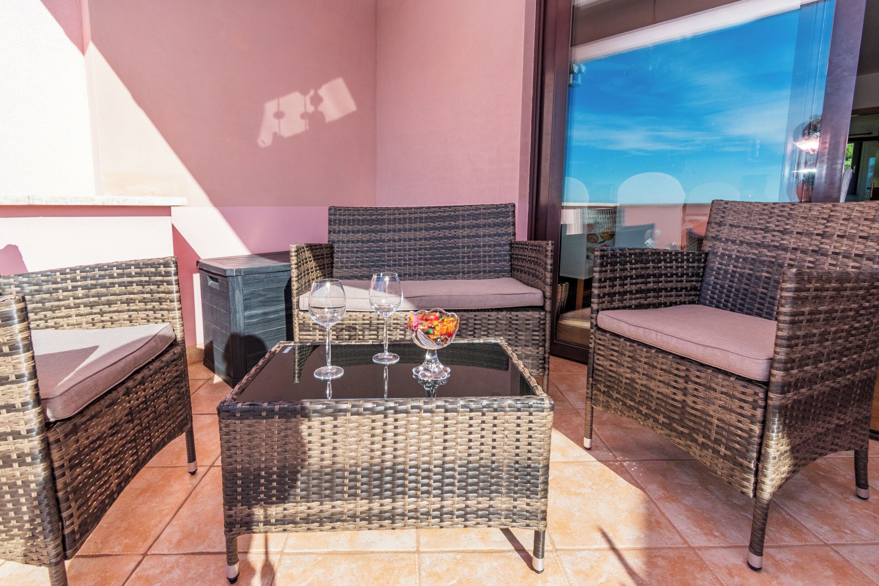 A balcony with wicker furniture, a glass table, and a bowl of fruit.