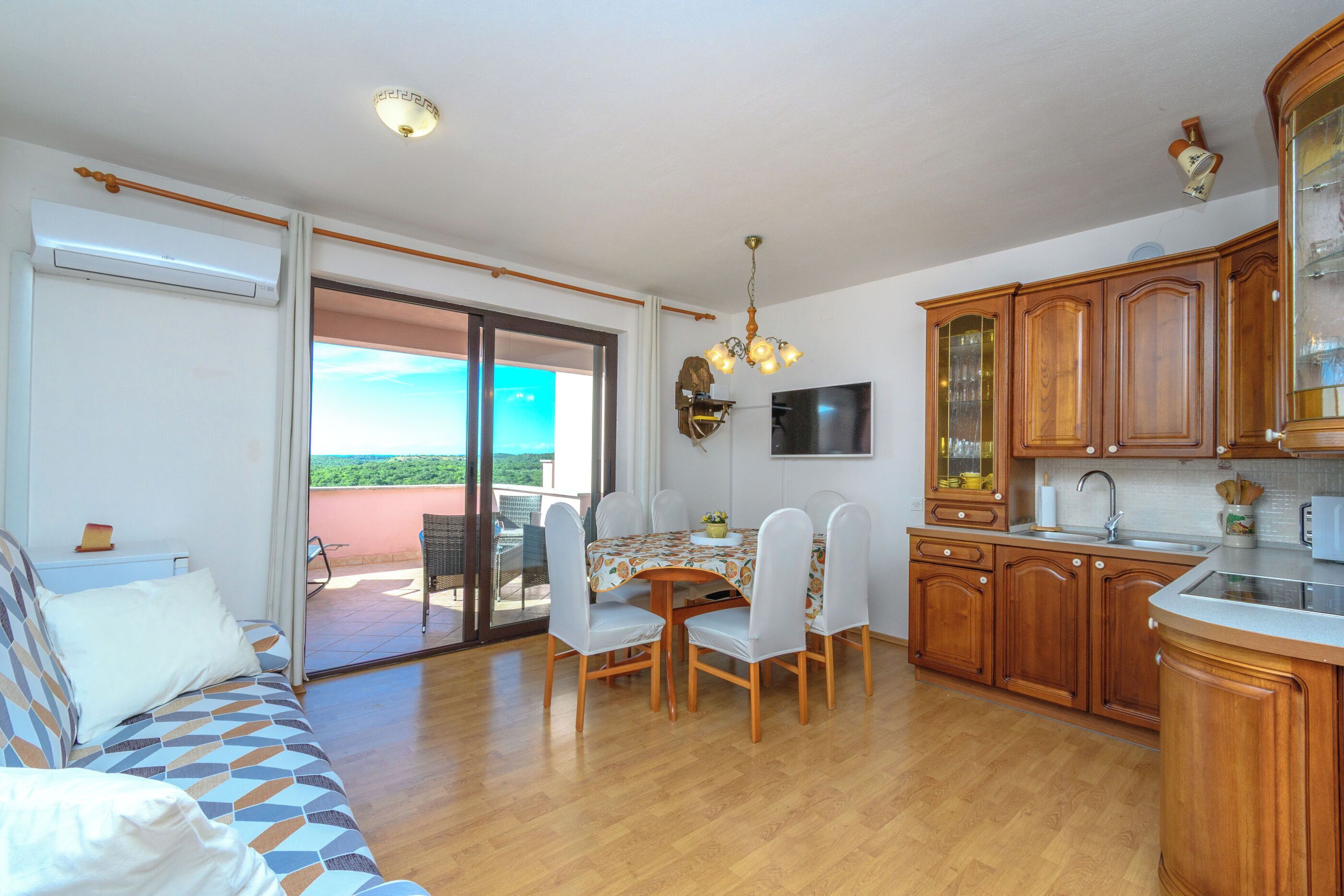 Eine moderne Küche mit Holzausstattung, einem Esstisch mit Stühlen, einem Fernseher und einem Balkon mit Blick.