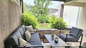 A patio area with a sofa, chairs, a table, and potted plants.