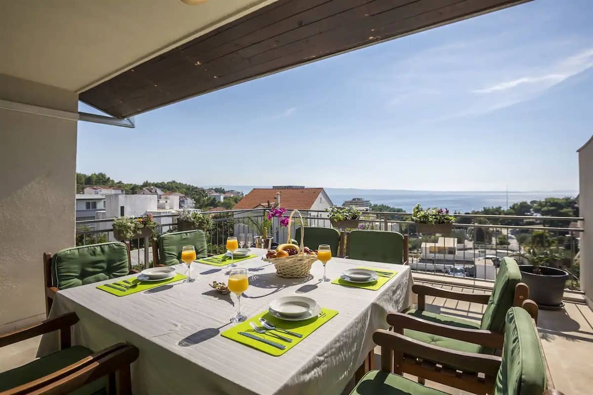 A balcony with a table set for two, overlooking a cityscape and the sea.