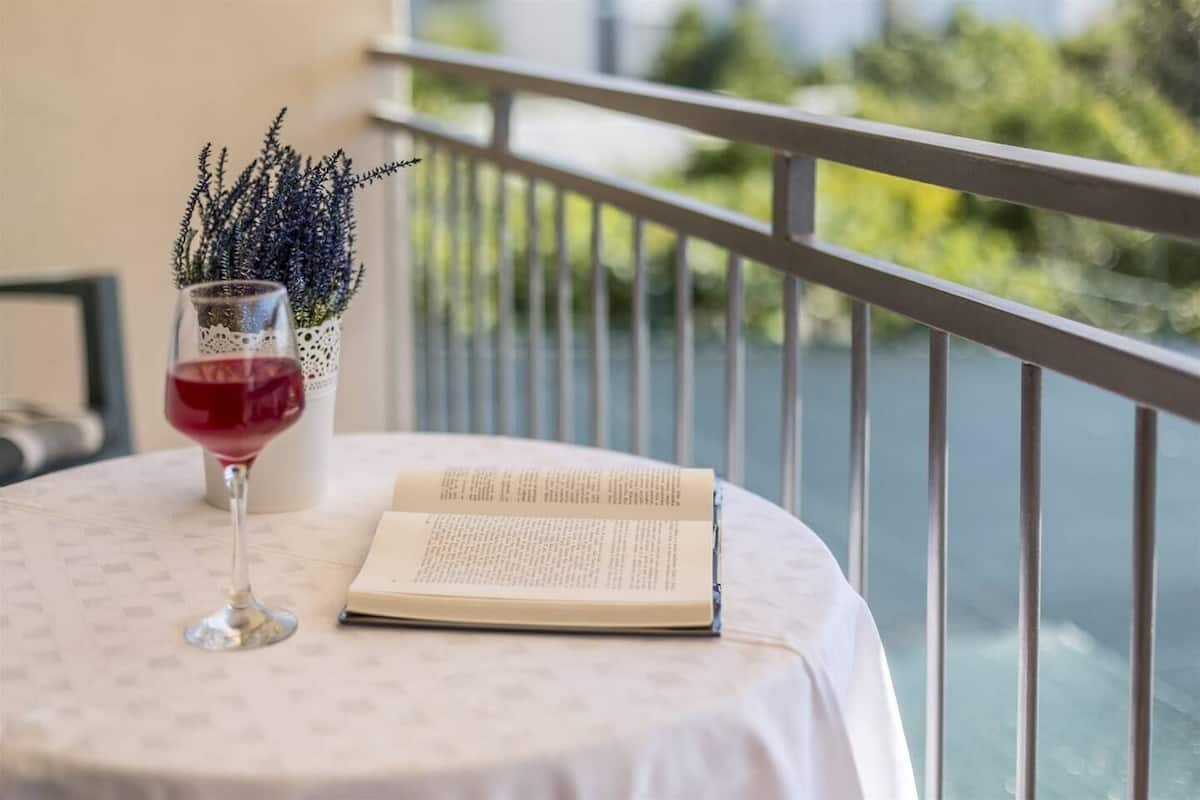 A table with a book and a glass of red wine, a potted plant, and a balcony railing.