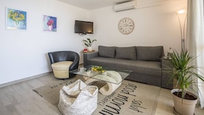 A modern living room with a sofa, a leather chair, a glass coffee table, a flat-screen TV, a wall clock, and a potted plant.