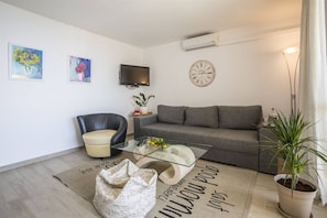 Ein modernes Wohnzimmer mit einer Couch, einem Ledersessel, einem Glastisch, einem Flachbildfernseher, einer Wanduhr und einer Topfpflanze.