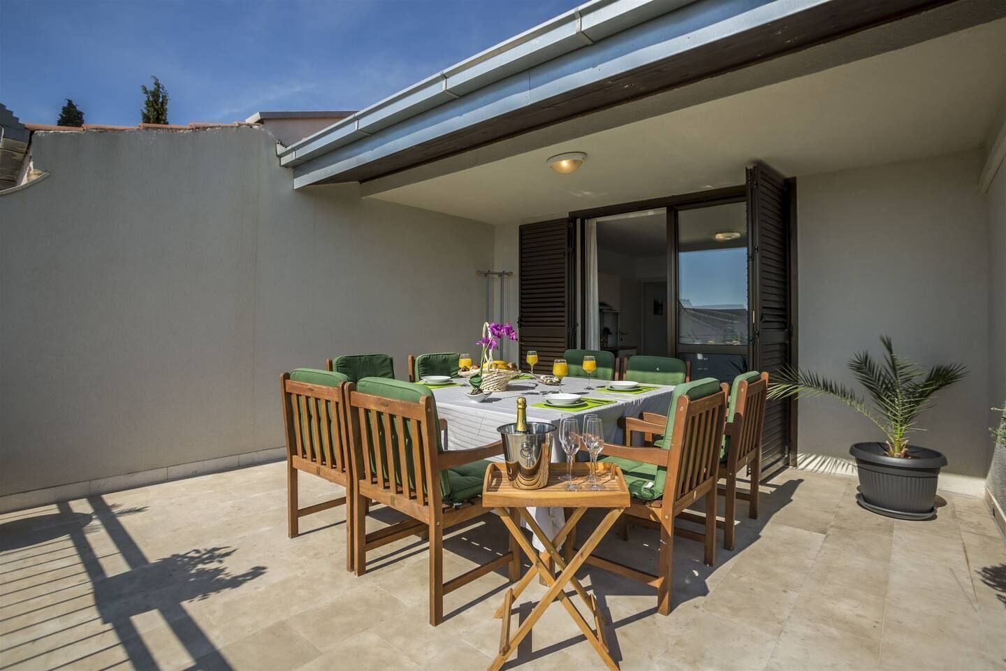 A patio with a table set for dining, surrounded by chairs, and a potted plant.