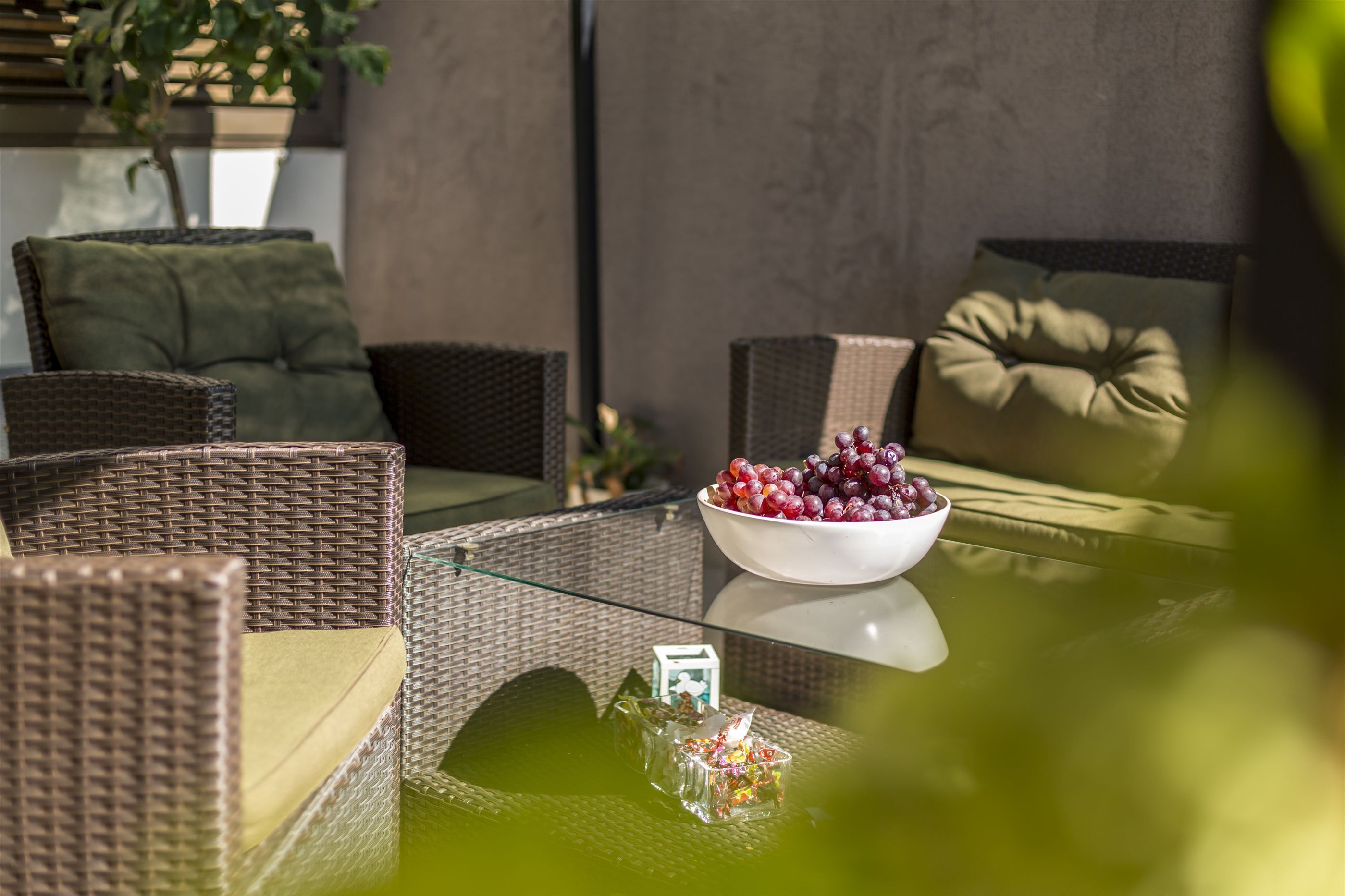A wicker sofa set with cushions, a glass table with a bowl of grapes, and a small decorative item.