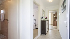 A hallway leading to a bedroom with a bed, a bedside table, and a mirror.