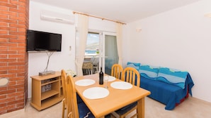 A room with a brick wall, a flat-screen TV, a wooden dining table with chairs, a sofa, and a window with curtains. - Apartments Sunce (Okrug)