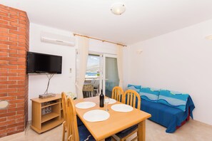 Ein Zimmer mit Backsteinwand, einem Flachbildfernseher, einem Holzesstisch mit Stühlen, einer Couch und einem Fenster mit Vorhängen.