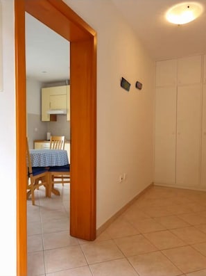Ein Zimmer mit Holzrahmen, gefliestem Boden, einem Essbereich mit Tisch und Stühlen sowie einem weißen Kleiderschrank.
