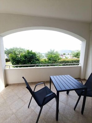 Ein Balkon mit Tisch und Stühlen, Blick auf Grünflächen und entfernte Gebäude.