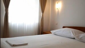 A hotel room with a bed, curtains, a nightstand, and a wall-mounted light. - Apartments Sunce (Okrug)