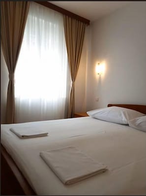 Ein Hotelzimmer mit Bett, Vorhängen, einem Nachttisch und einer Wandleuchte.