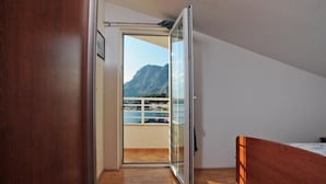 Ein Schlafzimmer mit einem hölzernen Bett, einer Schiebetür zu einem Balkon mit Blick auf die Berge.