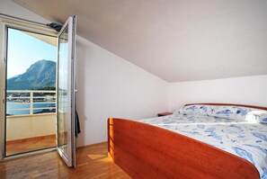 Ein Schlafzimmer mit einem hölzernen Bett, einer Glastür, die auf einen Balkon führt, und Blick auf Berge und Wasser.