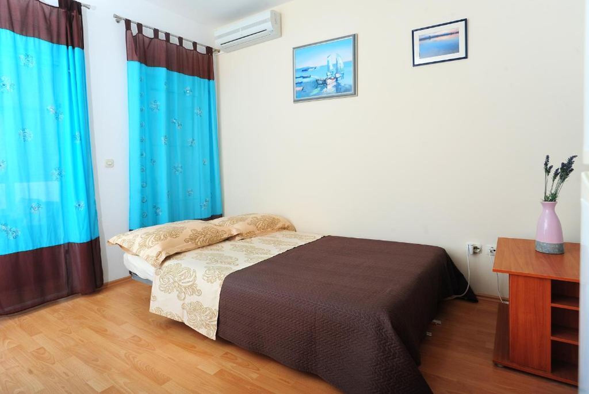 Un dormitorio con cama, cortinas, aire acondicionado instalado en la pared y dos cuadros enmarcados.