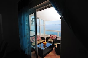 Ein Balkon mit Meerblick, eine Glastür und eine Sitzecke mit Kissen.