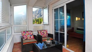 Ein Balkon mit Korbmöbeln, einem Glastisch und Blick auf Berge.