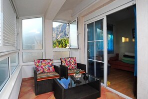 Ein Balkon mit Korbmöbeln, einem Glastisch und Blick auf Berge.