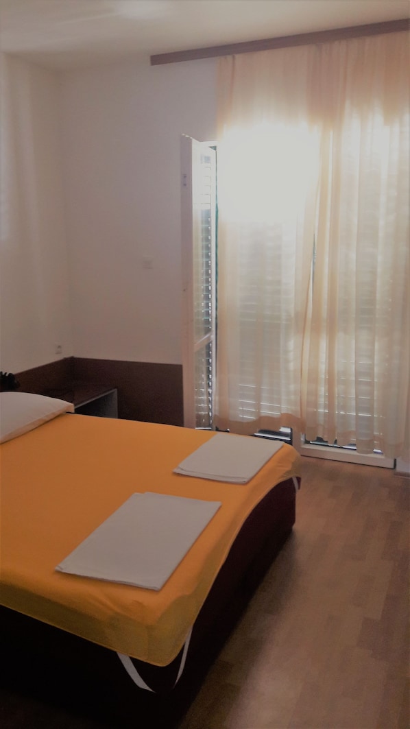A hotel room with a bed, a desk, a chair, a window with curtains, and a door. - Apartments Oliva (Sibenik)