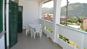 A balcony with a table and chairs, a view of buildings and hills, and green shutters. - Apartments Oliva (Sibenik)