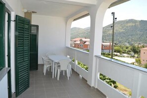 A balcony with a table and chairs, a view of buildings and hills, and green shutters. - Apartments Oliva (Sibenik)