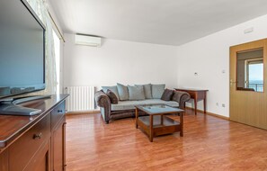 A modern living room with a sofa, coffee table, TV, and a view through a door. - Apartments Panorama (Crikvenica)